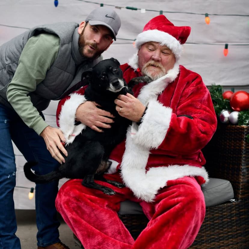 Santa posing with a black dog and its owner on the patio
